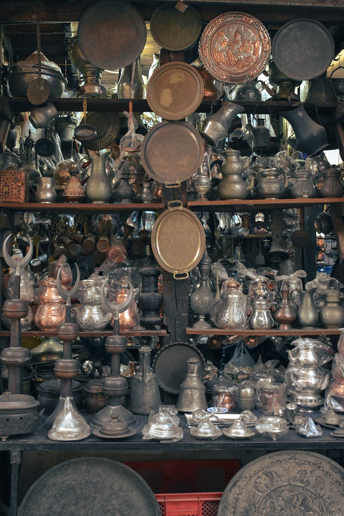 A diverse collection of antique metalware items on display at a bustling market stall.
